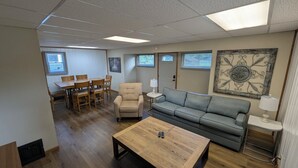 Un salon meublé comprenant une table basse en bois, un canapé gris, un fauteuil beige et une table à manger avec des chaises.
