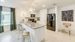 A modern kitchen with a central island, bar stools, stainless steel appliances, and a decorative ceiling light. - ~ 10 Mi to Dallas Hospitals: Stylish Home w/ Yard! (Dallas)