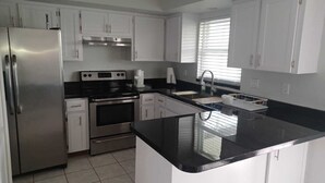 A modern kitchen with white cabinets, stainless steel appliances, and a black countertop. - 10 min. from the beach, pet-friendly, fenced yard. (Englewood)