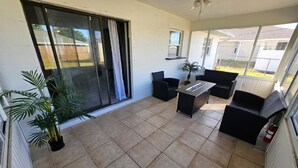 A patio area with a sliding glass door, black wicker furniture, a small table, and a potted plant. - 10 min. from the beach, pet-friendly, fenced yard. (Englewood)