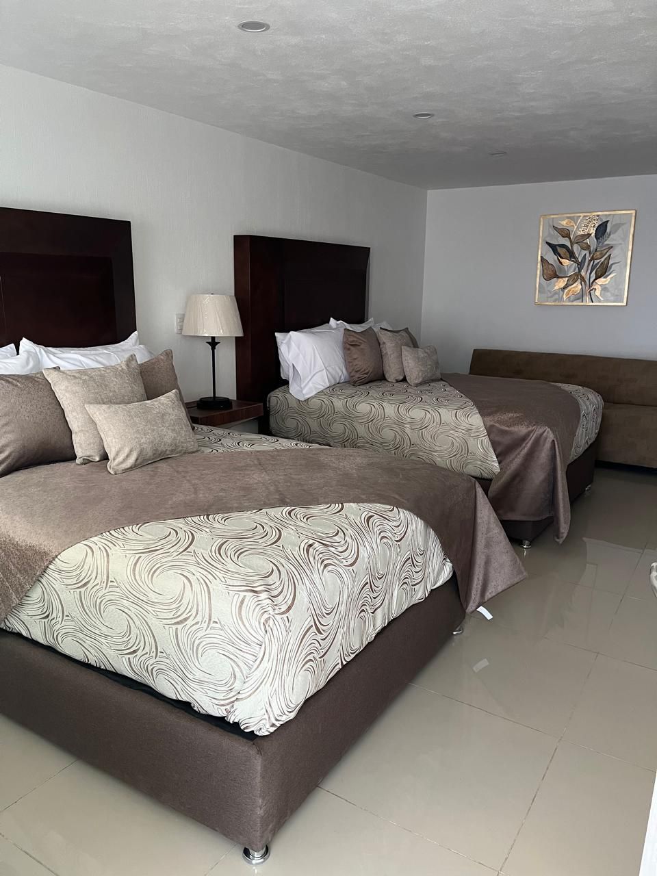 A hotel room with two beds, each with a headboard, a nightstand with a lamp, and a wall-mounted artwork.