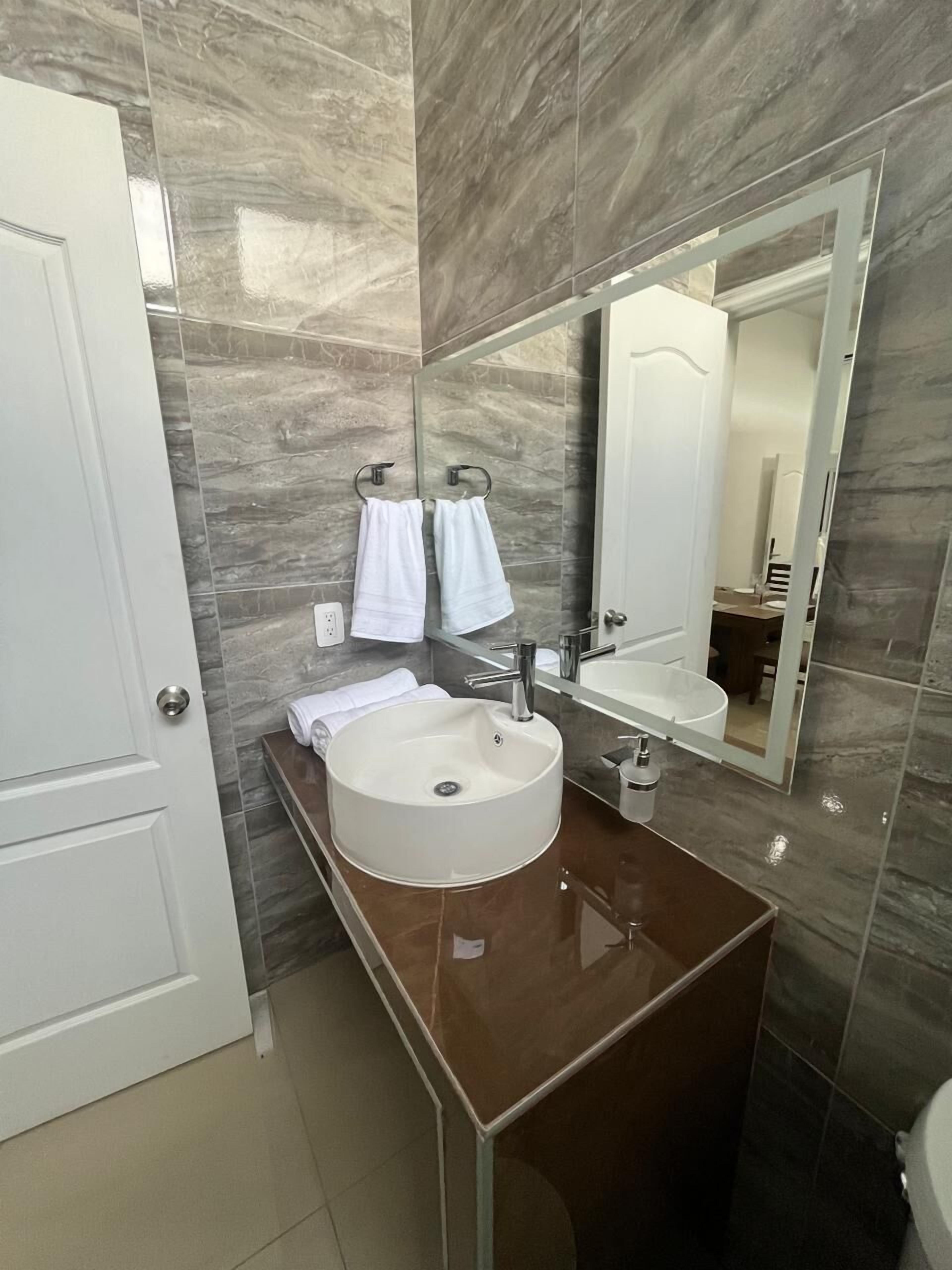 A modern bathroom with a round sink, a large mirror, and two towels hanging on hooks.