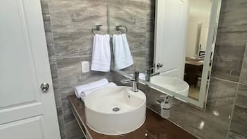 Un baño moderno con un lavamanos redondo, un espejo grande y dos toallas colgadas de ganchos.