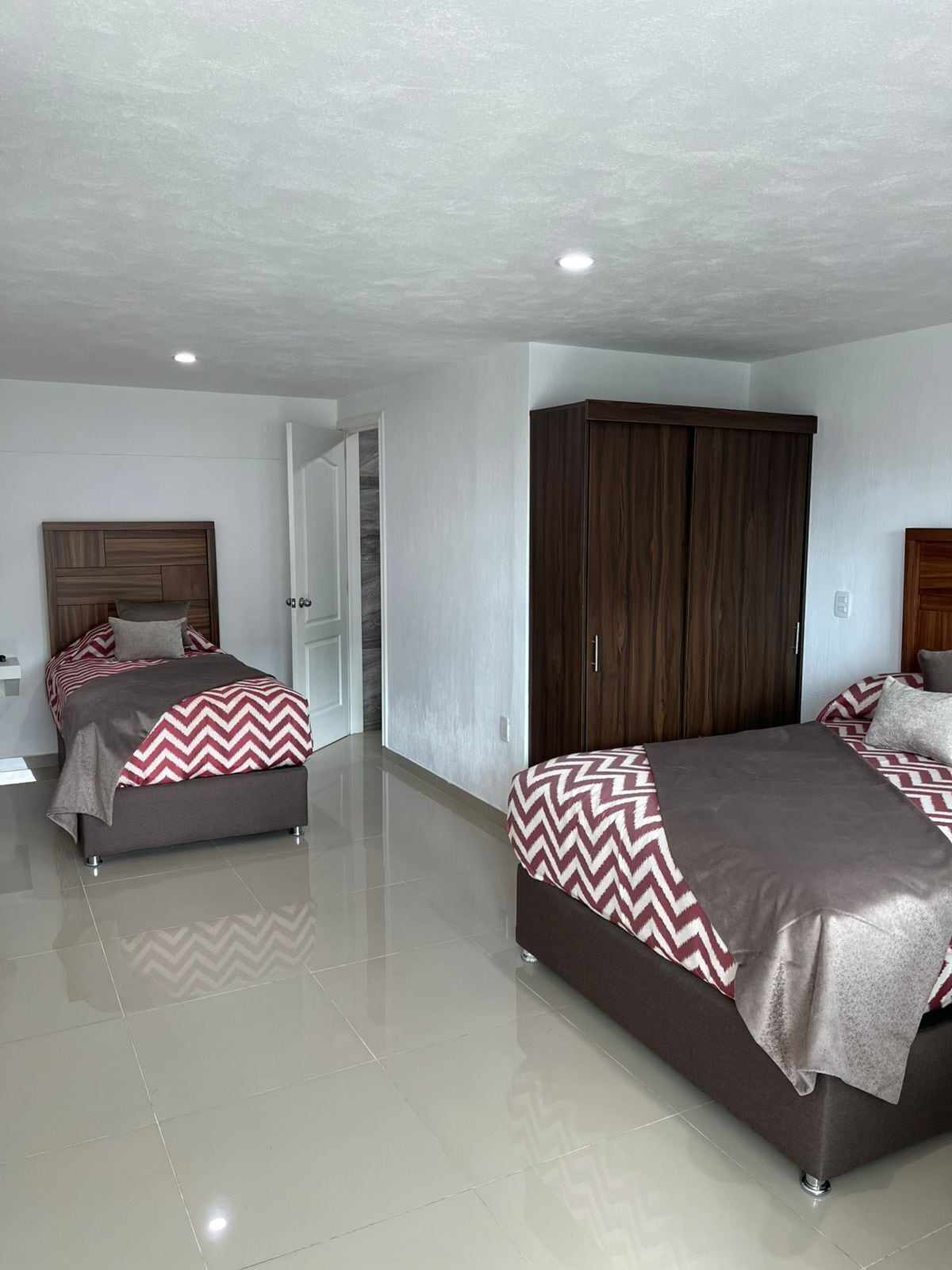 A modern bedroom with two beds, a wardrobe, and a bathroom.