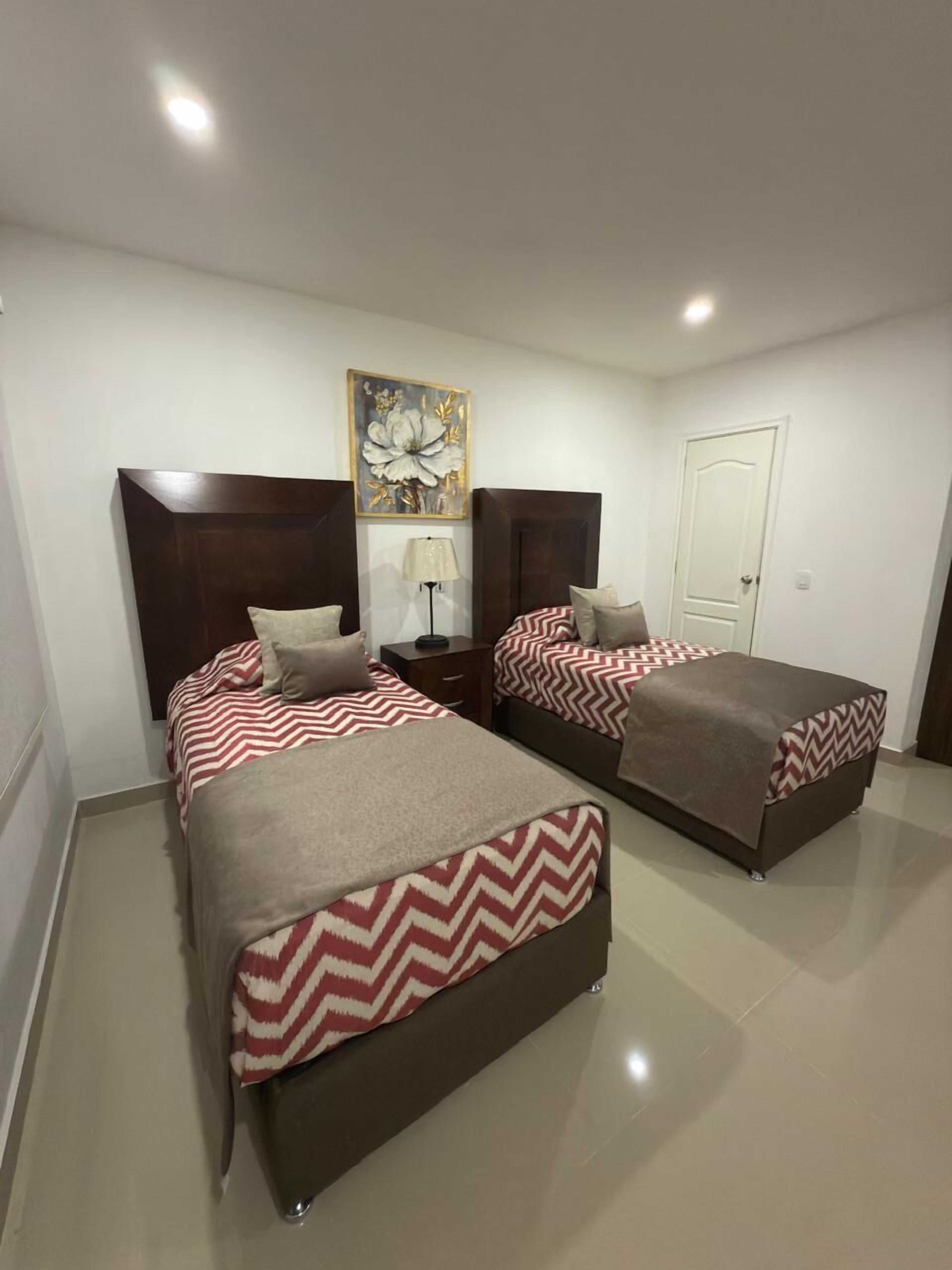 A hotel room with two beds, a nightstand, a lamp, and a door.