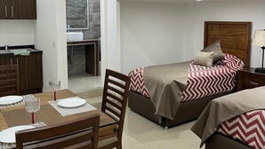 Ett modernt och kompakt hotellrum med en matplats, två sängar med mönstrat sänglinne, ett litet pentry och ett badrum med spegel och handfat.