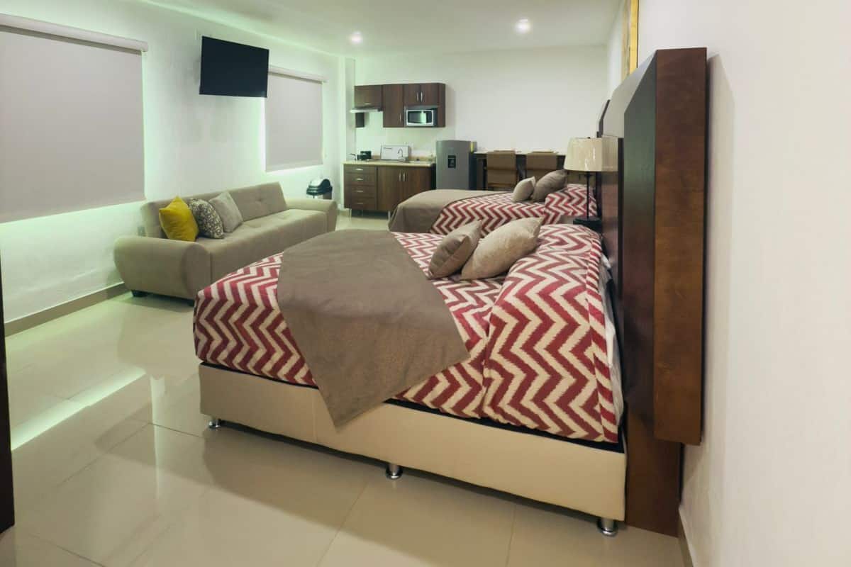 Un dormitorio moderno con una cama grande, un sofá y una kitchenette al fondo.