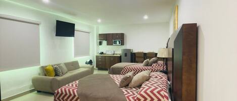Un dormitorio moderno con una cama grande, un sofá y una kitchenette al fondo.
