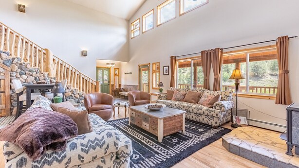 A spacious living room with a high ceiling, a stone staircase, and large windows offering a view of the outdoors.