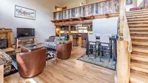 A spacious living area with a high ceiling, wooden staircase, and a dining area with a bar.
