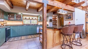 A kitchen with teal cabinets, a wooden ceiling, and a bar area with stools.
