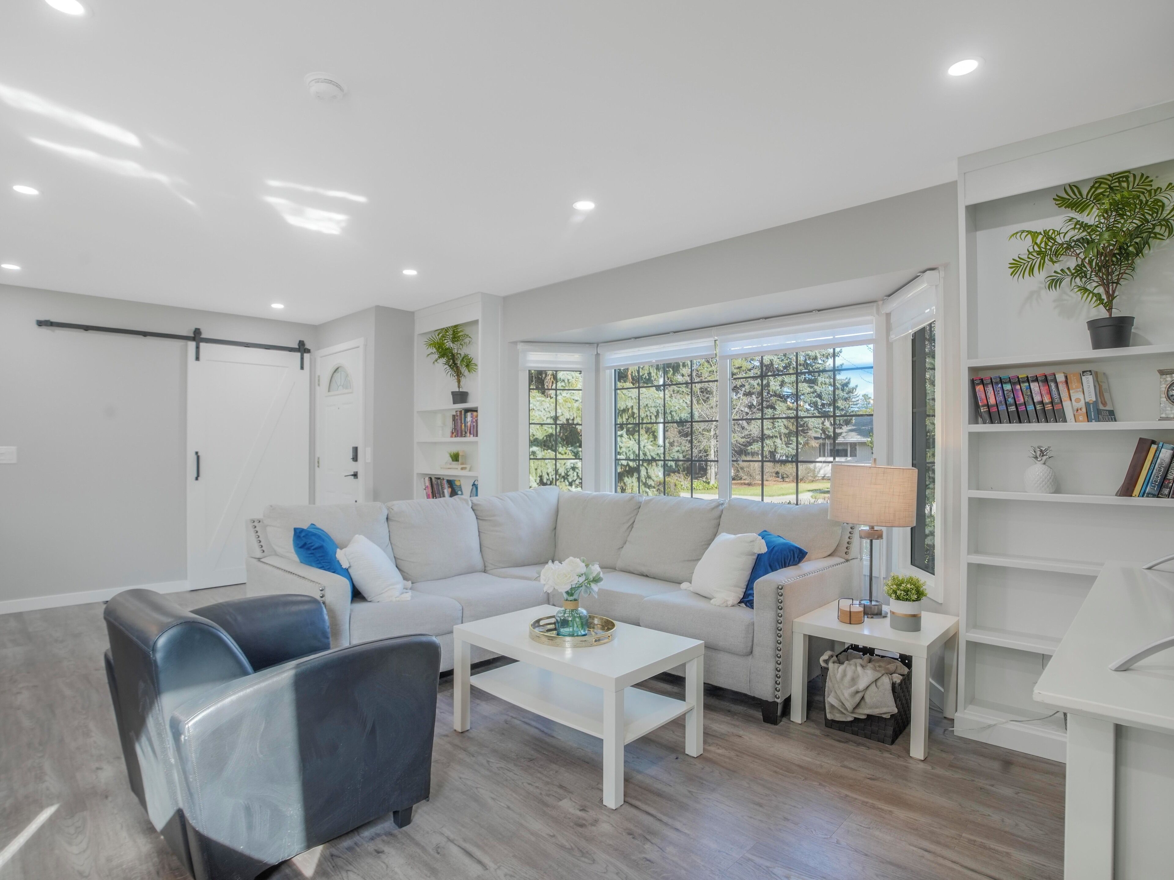 A modern living room with a sofa, two armchairs, a coffee table, and a bookshelf.