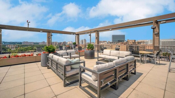 Eine Dachterrasse mit Sitzgelegenheiten im Freien, Blumentöpfen und Blick auf die Stadt.