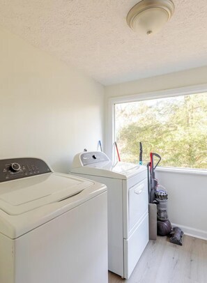 A laundry area with a washing machine, dryer, and a window with a view of trees.