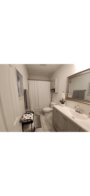 Un baño con inodoro, ducha, lavabo y una pequeña mesa con toallas.