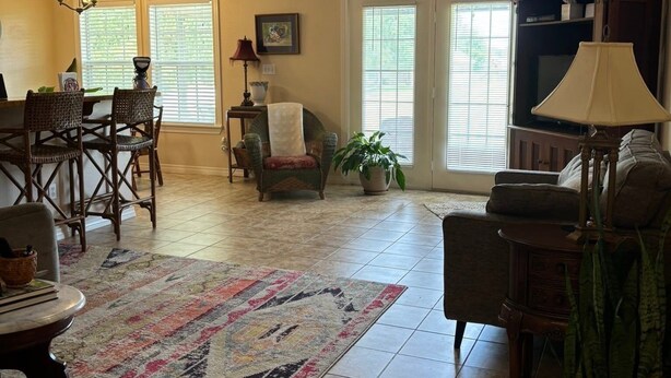 A spacious living room with a large rug, a dining area with chairs, a ceiling fan, and a potted plant.
