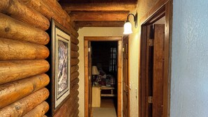 Ein Holzblockhaus-Innenraum mit einer Holzwand, einem gerahmten Bild, einer Lampe und einer Tür zu einem anderen Raum.