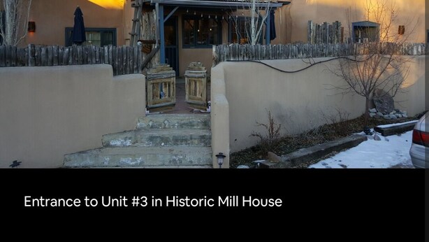 The entrance to Unit #3 in a historic mill house with a wooden fence, steps leading up to the door, and a snow-covered ground. - Historic Mill House Unit 3 (Taos)