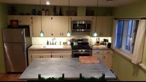 A compact kitchen with a refrigerator, microwave, stove, and sink. There is a table with chairs and a window with curtains. - Historic Mill House Unit 3 (Taos)