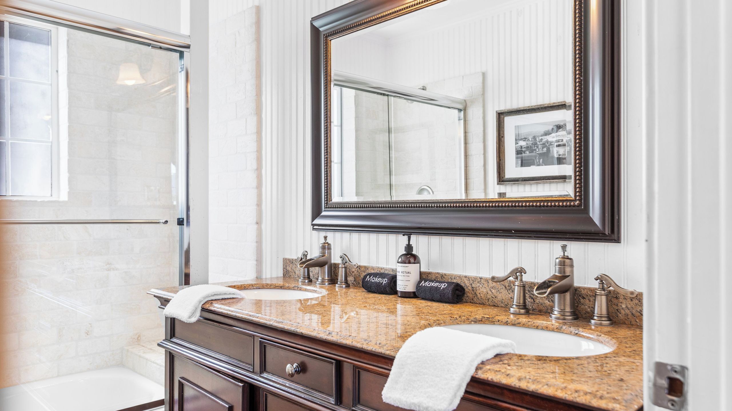 A bathroom with a large mirror, two sinks, a vanity with drawers, and a towel rack.