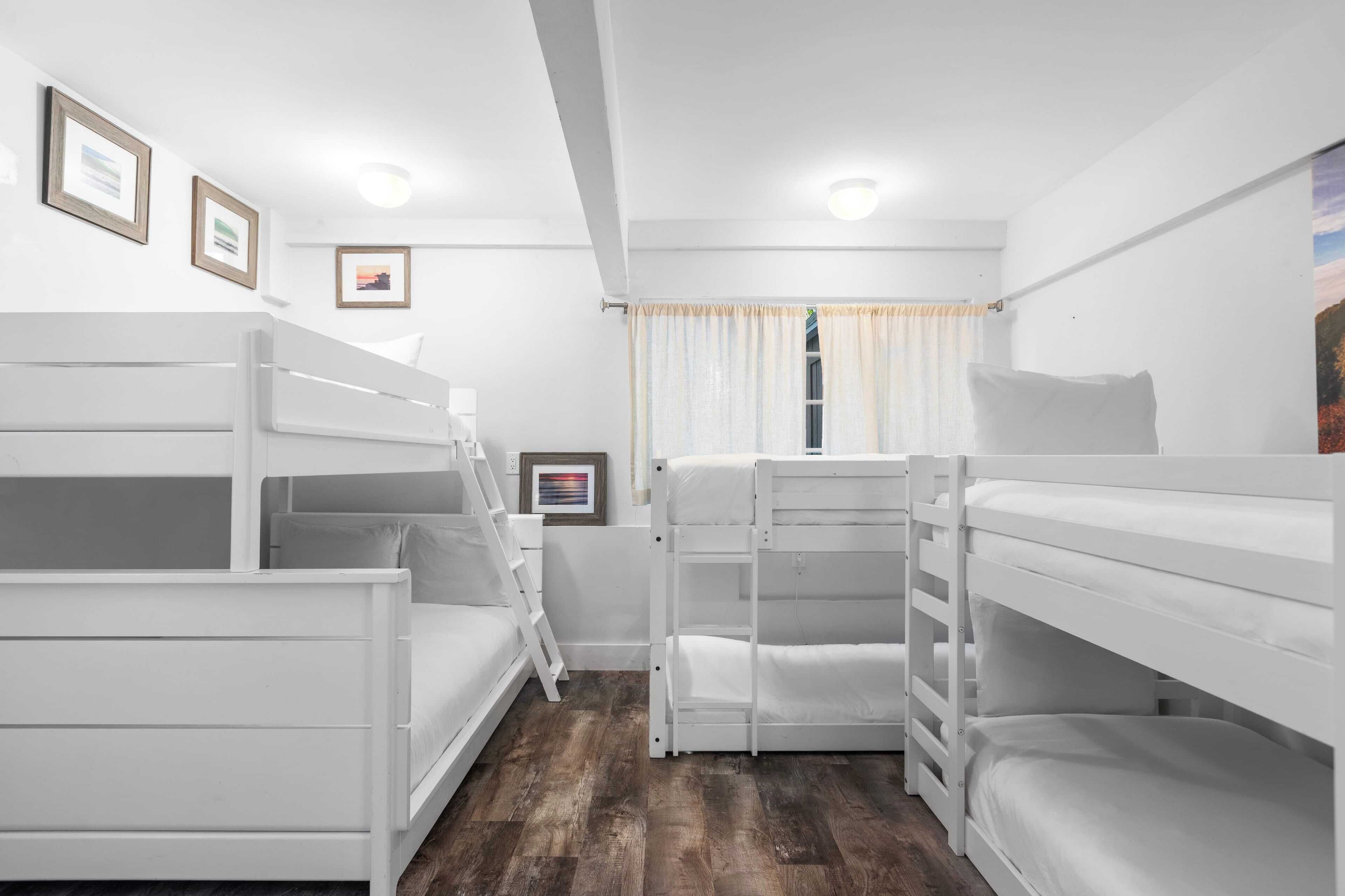 A room with bunk beds, a ladder, a window with curtains, and framed pictures on the wall.