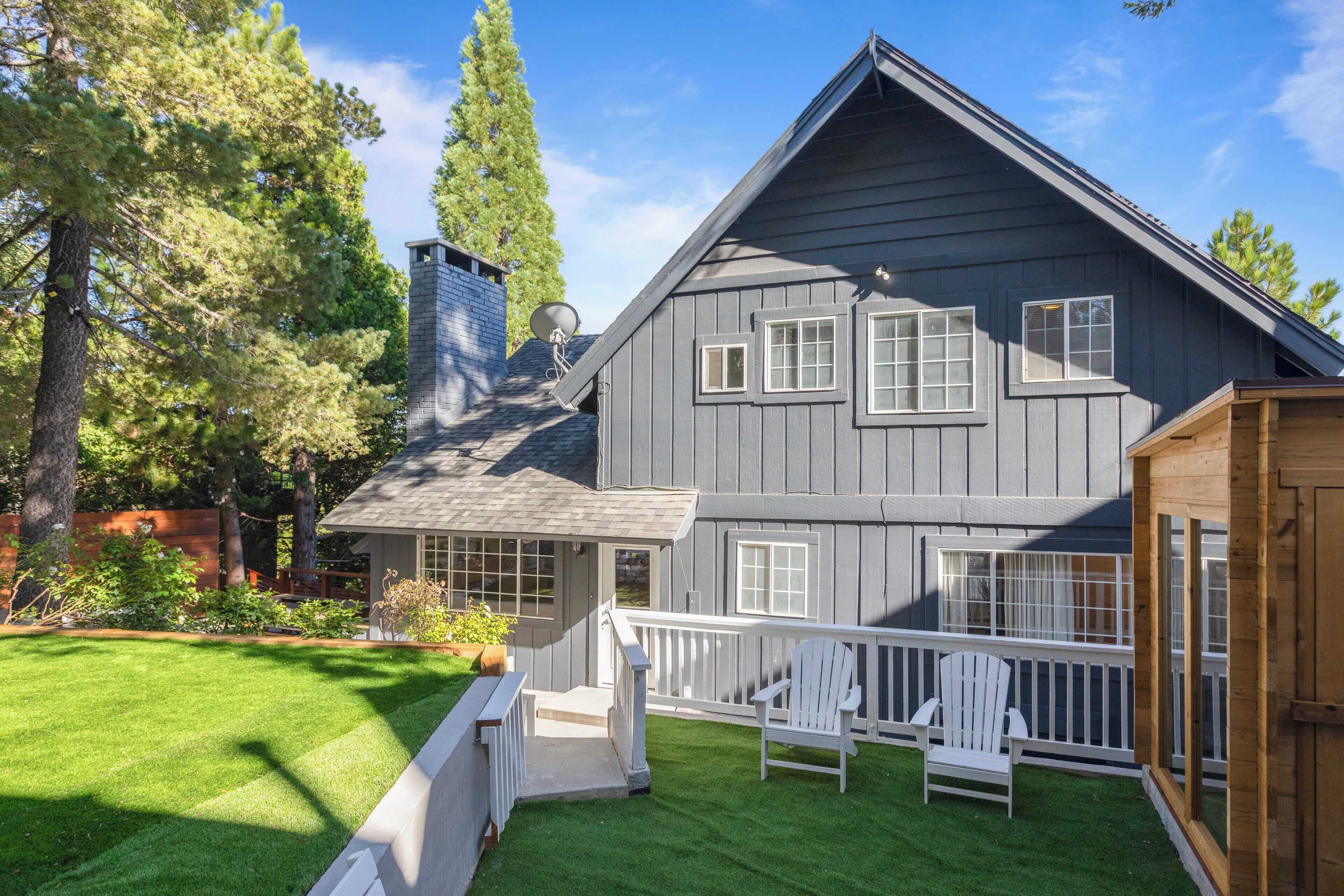 A two-story house with a grey exterior, a wooden deck, and a white railing.