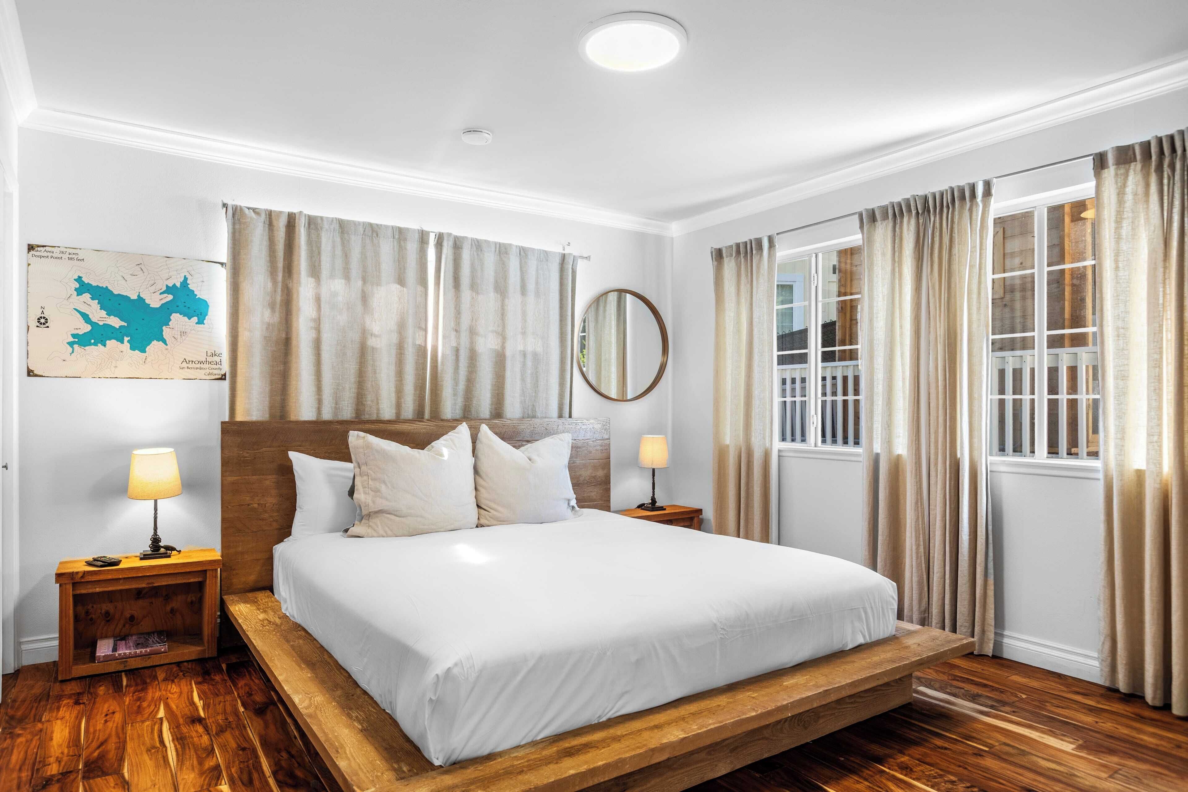 Een ruime slaapkamer met een groot bed, een houten hoofdbord, twee nachtkastjes met lampen, een kaart aan de muur en een raam met gordijnen.