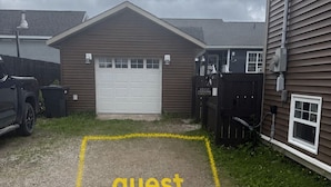 Un estacionamiento de grava señalizado como 'estacionamiento para huéspedes' con un edificio al fondo.