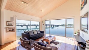 Un salón amplio con un gran ventanal que da a un lago tranquilo y un puente.