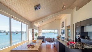 Una cocina moderna con una isla grande, un comedor con banco y vistas a un puente sobre el agua.