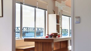 Una habitación de hotel moderna con una cama grande, muebles de madera, una zona de comedor con vistas a un puente y un ventanal amplio.