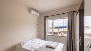 Une chambre d’hôtel avec un lit, une fenêtre avec des rideaux et un climatiseur fixé au mur.