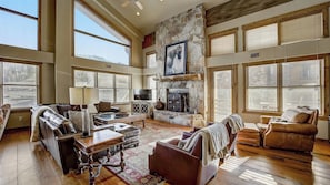 A spacious living room with a stone fireplace, leather sofas, a television, and large windows. - 7 Condos, Ski-in/ski-out + Hot Tubs Sleeps 30 Mont Cervin by Avantstay (Park City)
