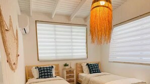 A room with two beds, a hanging light fixture, and a window with blinds.