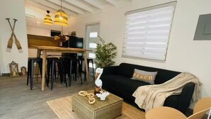 A living room with a sofa, coffee table, and chairs, a dining area with a table and chairs, and a kitchen in the background.