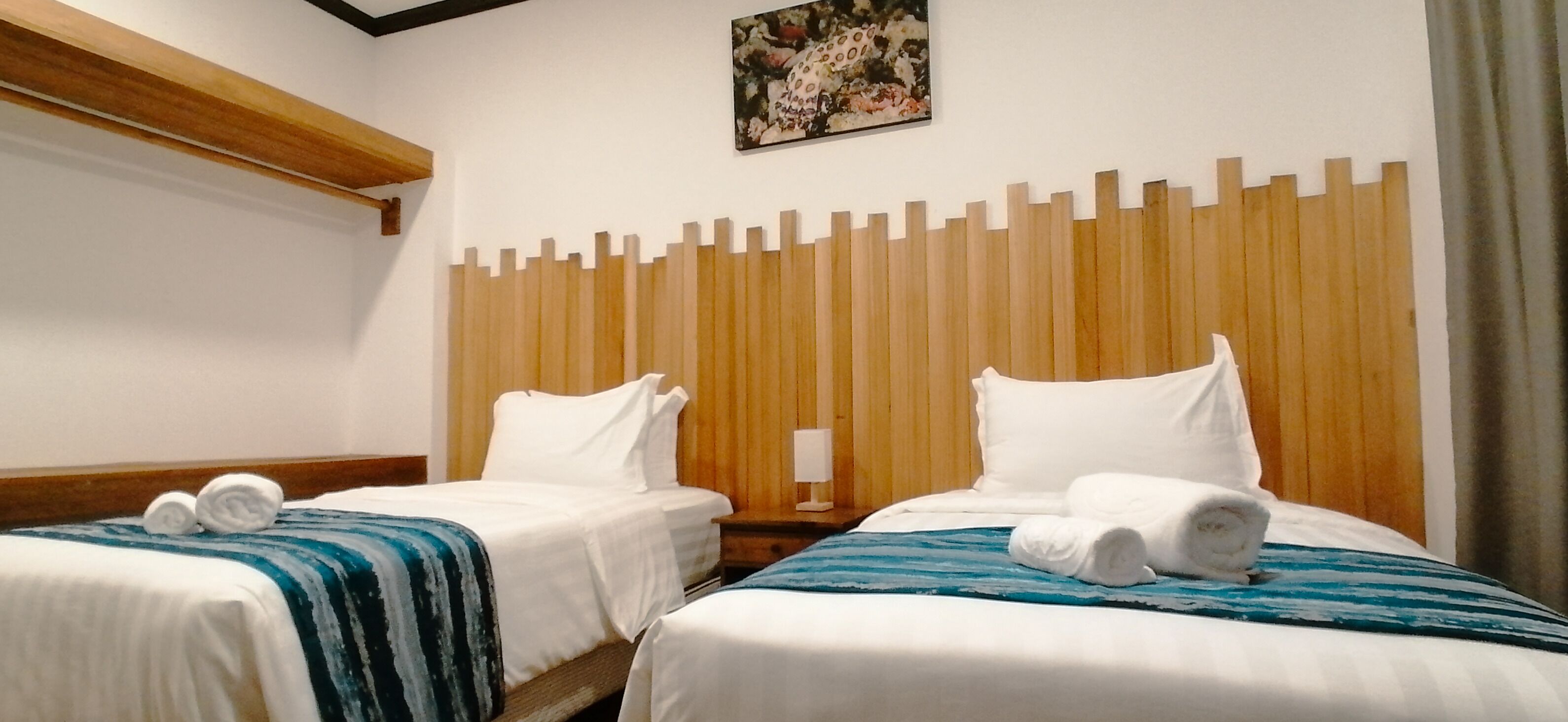 Habitación de hotel con dos camas, cabecero de madera, ropa de cama blanca y un cuadro en la pared.