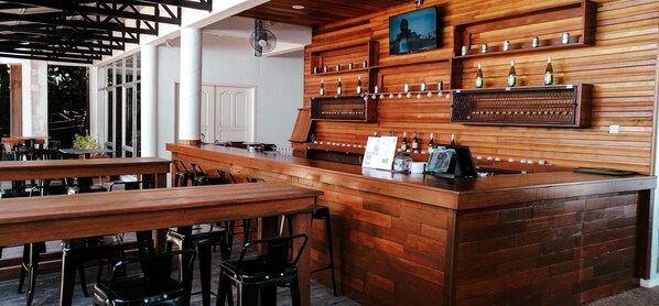 Un espace bar avec des meubles en bois, un comptoir où sont exposées des bouteilles et un téléviseur fixé au mur.