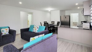 Ein modernes Wohnzimmer mit einer Couch und Sesseln, einem Esstisch und einer Küchenzeile mit Kühlschrank und Mikrowelle.