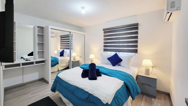 Ein Schlafzimmer mit einem Bett, Nachttischen, einem Kleiderschrank, einem Spiegel und einer Deckenleuchte.
