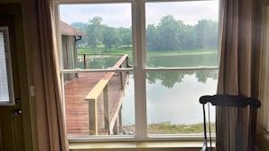A room with a large window overlooking a lake, a wooden deck, and a chair. - The Moose Lodge on the Susquehanna River (Sugar Run)