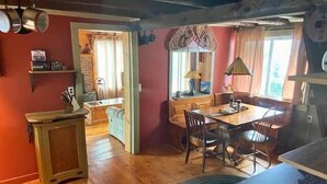A cozy kitchen with wooden cabinets, a dining table, and a window with curtains. - The Moose Lodge on the Susquehanna River (Sugar Run)