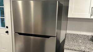 Ein Edelstahl-Kühlschrank in einer Küche mit weißen Schränken und einer Arbeitsplatte aus Granit.