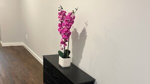 Eine schwarze Kommode mit Schubladen vor einer weißen Wand, eine Orchidee im Topf darauf und ein Holzboden.