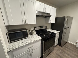 A kitchen with white cabinets, a stainless steel refrigerator, a microwave, a stove, and a toaster.