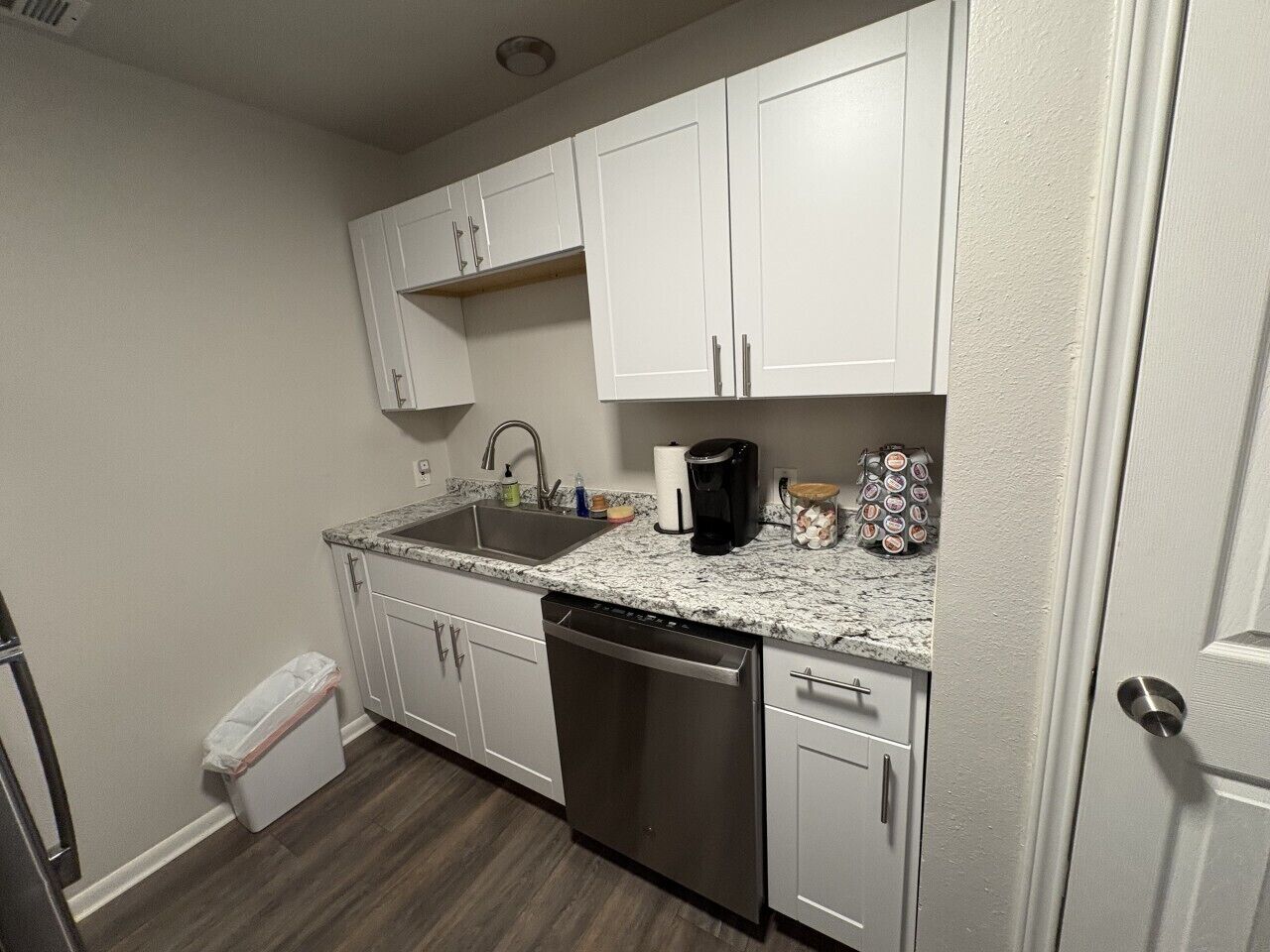 A compact kitchen with white cabinets, a stainless steel dishwasher, and a granite countertop.
