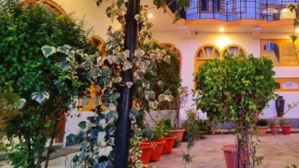 A covered outdoor area with potted plants and a building with arched windows and balconies. - Hotel Surya International - Manali (Manali)