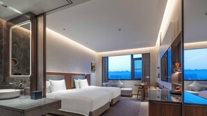 Une chambre d’hôtel moderne dotée d’un grand lit, d’un coin salon, d’un bureau et d’une salle de bain avec un grand miroir.