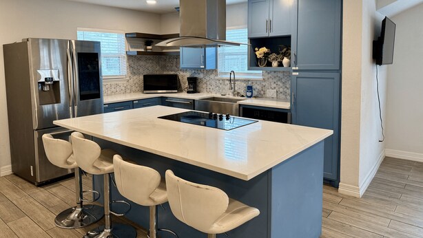 A modern kitchen with a central island, bar stools, stainless steel appliances, and blue cabinetry. - 3rd Ward Gem: Modern Comfort + History (Houston)