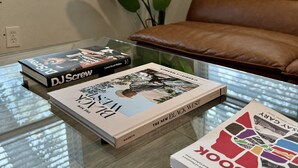 A living room with a glass coffee table holding books, a brown leather sofa, and a large green plant. - 3rd Ward Gem: Modern Comfort + History (Houston)