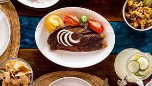 Ein Teller gegrillter Fisch mit Zitronenscheiben, Tomaten und Zwiebeln, dazu eine Salatschüssel und ein Spießteller.